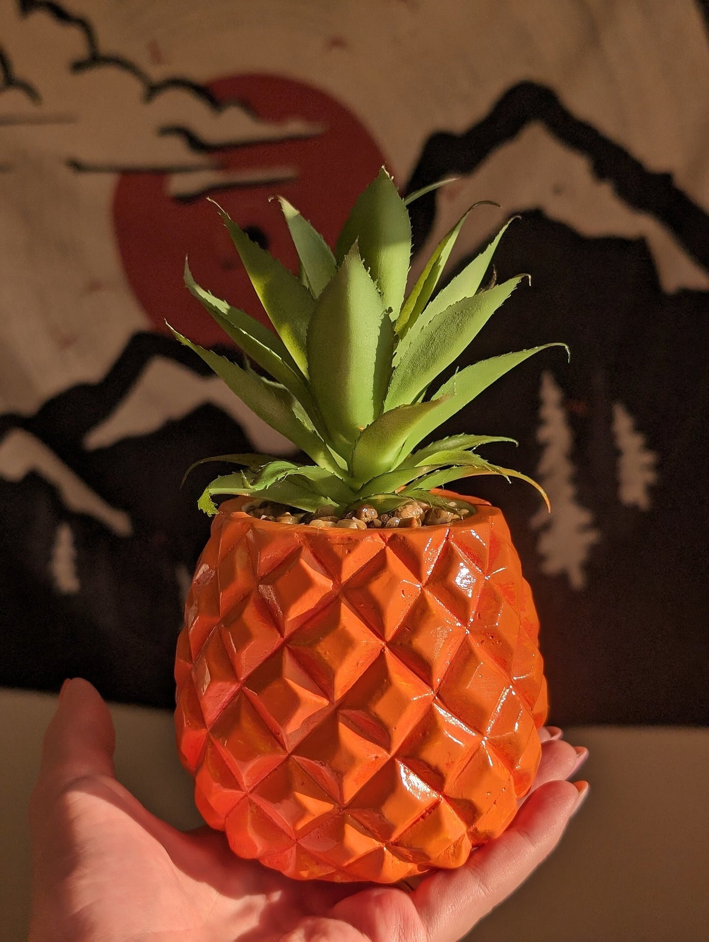 bright orange pinapple succulent held up in sunlight in front of pop art tapestry