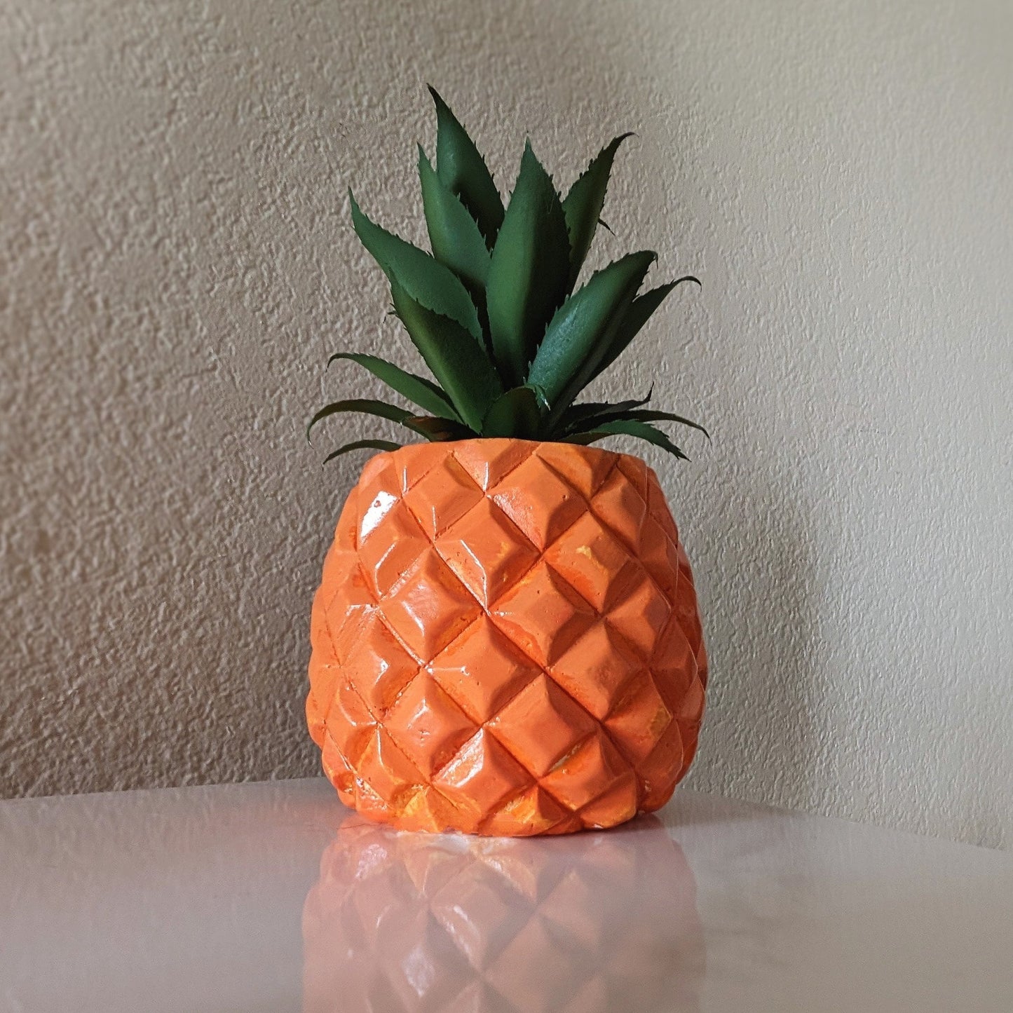 bright orange pinapple succulent on a smooth white desk with its reflection showing below